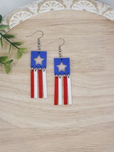 red, white and blue earrings with stars on them sitting on a table next to a plant