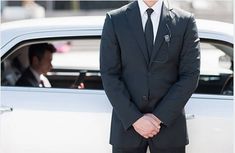 a man in a suit and tie standing next to a white car with a stethoscope on his ear