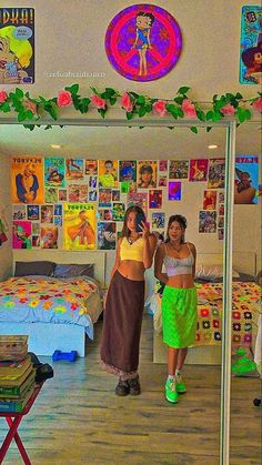 two women are standing in a room with posters on the wall and bedspreads