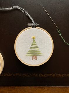 two different types of embroidery are on the table next to scissors and thread, one with a christmas tree in it