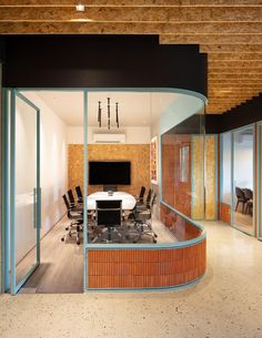 a conference room with glass walls and wooden ceilinging, along with an oval table surrounded by black chairs