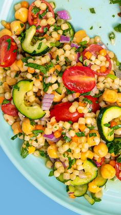 a salad with corn, cucumbers, tomatoes and green onions on a blue plate