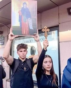 two people holding up crosses in front of a sign with the image of jesus on it