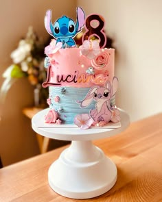 a pink and blue birthday cake with lil the little mermaid characters on it sitting on a table