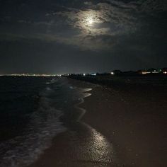 the moon is shining over the water at night on the beach with waves coming in