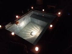 candles are lit around an empty swimming pool in the middle of dark room with lights on it