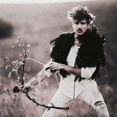 a man holding a bow and arrow while standing in a field with wildflowers