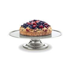 a cake with berries and nuts on top sitting on a silver platter in front of a white background