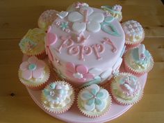 a birthday cake decorated with cupcakes on a pink plate and wooden table top