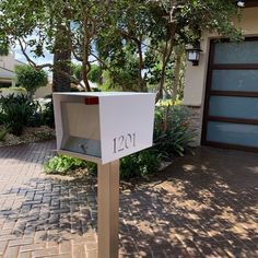 a white mailbox sitting on top of a brick walkway next to a tree and bushes