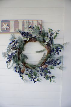 a wreath is hanging on the wall with pine cones and blue berries in front of it