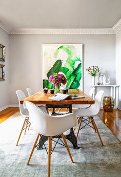 a dining room table with white chairs and a painting on the wall