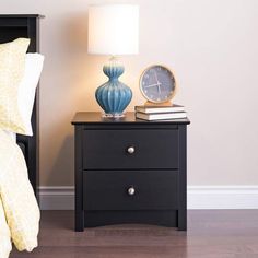 a night stand with two drawers and a clock on it, next to a bed