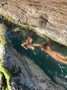 two people are swimming in the water near some cliffs