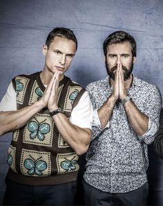 three men standing in front of a blue wall with their hands together and one man covering his mouth