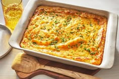 a casserole with cheese and herbs in a white dish next to a wooden spoon