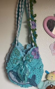 a crocheted purse hanging on the wall next to a stuffed animal and heart shaped mirror