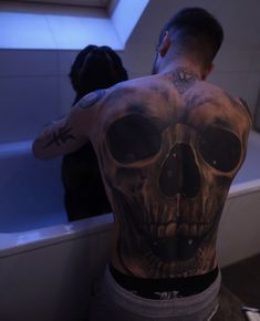 a man with a skull tattoo on his back standing in front of a bathtub