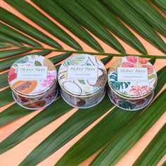 three tins of lip bales sitting on top of a palm leaf next to each other