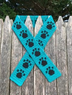 a blue crocheted scarf with black paw prints on it sitting on a wooden fence