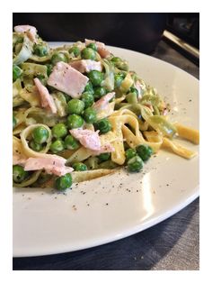 a white plate topped with pasta covered in peas and ham meats on top of it