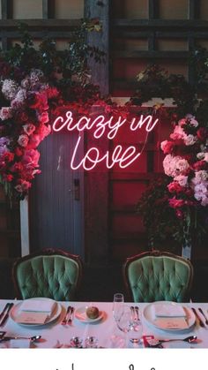 a table set for two with pink flowers and greenery in the background that says crazy in love