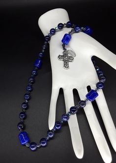 The Deep Blue Irish Anglican Rosary is a beautiful rosary that radiates the seven seas and provides you with a calming effect while praying. The rosary is made of Swarovski Crystals, Lapis lazuli and Jade gemstones (which have been cleansed and purified) while a Stainless Silver Cross completes the rosary. Finally, the rosary has been blessed by the church. Rosary: Anglican configuration Blessed: Yes About the Rosary: The Rosary has a Cross, an Invitatory bead, 4 sets of 7 beads that are called Blue Spiritual Rosary With Gemstone Beads, Spiritual Blue Rosary With Gemstone Beads, Blue Gemstone Beads Rosary For Spiritual Use, Blue Spiritual Cross Jewelry, Blue Cross Spiritual Jewelry, Blue Crucifix Necklace For Spiritual Wear, Blue Crucifix Necklace For Spiritual Purposes, Handmade Blue Crucifix Jewelry, Blue Cross Spiritual Necklace