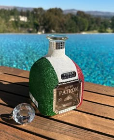 a bottle of liquor sitting on top of a wooden table next to a body of water