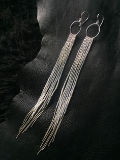 two white tassels hanging from a pair of silver hoop earrings on a black leather surface