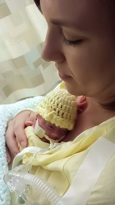 a woman holding a baby wearing a yellow knitted hat and looking at the camera