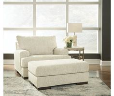 a white chair and ottoman in front of a large window with flowers on the table