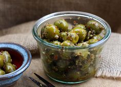 a glass jar filled with green olives next to a small bowl full of pickles