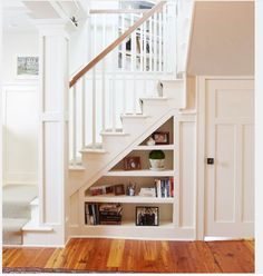 there is a bookshelf under the stairs in this house with white walls and wood floors