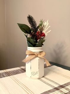 a mason jar filled with flowers and greenery sitting on top of a checkered table cloth