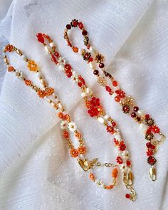 three necklaces are laying on top of a white cloth with beads and charms hanging from them