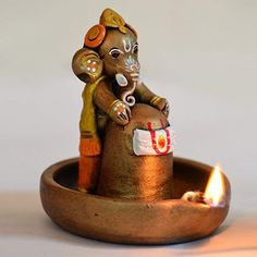 a small figurine sitting on top of a pot with a lit candle in it