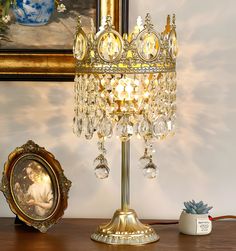 a gold colored table lamp with crystal beads on it and a framed painting in the background