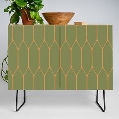 a plant is sitting on top of a green cabinet with geometric design and metal legs