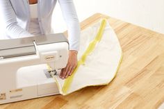 a woman is using a sewing machine to sew something on a wooden table top