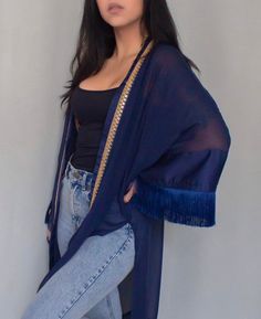 Dark blue oversized kimono with fringe details on the sleeves and an embroidered trim detail.  This kimono was made for those who live life on the go. The oversized silhouette makes it perfect for those long days exploring new cities or lounging at the beach. The fringe and embroidered trim add a touch of fun and personality, while the side slits make it easy to move around. Whether you're packing it for your next trip or wearing it around town, this kimono will make you feel like the wanderlust Festival Long Sleeve Kimono With Fringe, Long Sleeve Festival Kimono With Fringe, Long Sleeve Fringe Kimono For Festivals, Spring Kaftan With Tassels And Kimono Sleeves, Fall Beach Kimono With Tassels, Bohemian Festival Kimono With Tassel Ties, Bohemian Long Sleeve Kimono With Fringe, Summer Shawl With Tassels, Traditional Spring Kaftan With Tassels