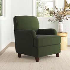 a green chair sitting in front of a window next to a vase with flowers on it