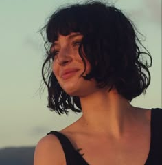 a close up of a person wearing a black shirt and smiling at the camera with mountains in the background