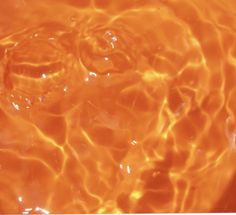 an orange substance floating on top of water in a bowl with bubbles and ripples