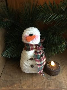 a snowman sitting next to a pine tree with a lit candle in front of it