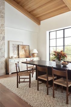 a dining room table with four chairs and a vase on top of it in front of a large window