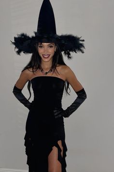 a woman in a black dress and hat with feathers on her head posing for the camera