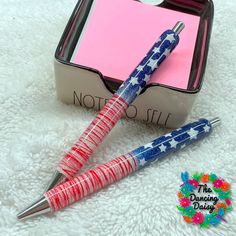 two red, white and blue pens sitting on top of a pink note pad next to a pen holder