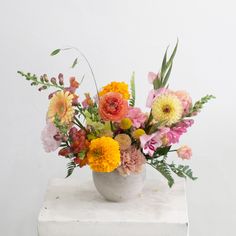 a white vase filled with lots of different colored flowers on top of a marble block