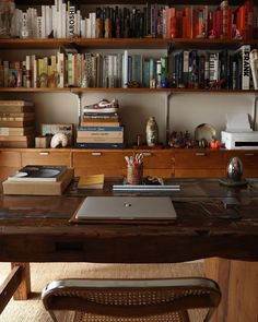 a wooden desk topped with a laptop computer next to a book shelf filled with books