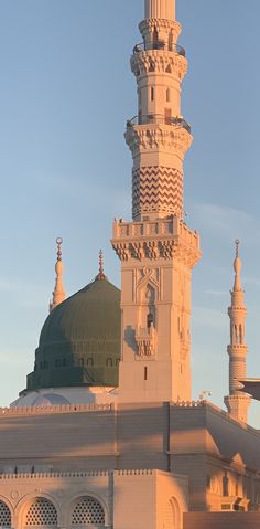 a tall white building with a green dome and two minalis on top, in front of a blue sky